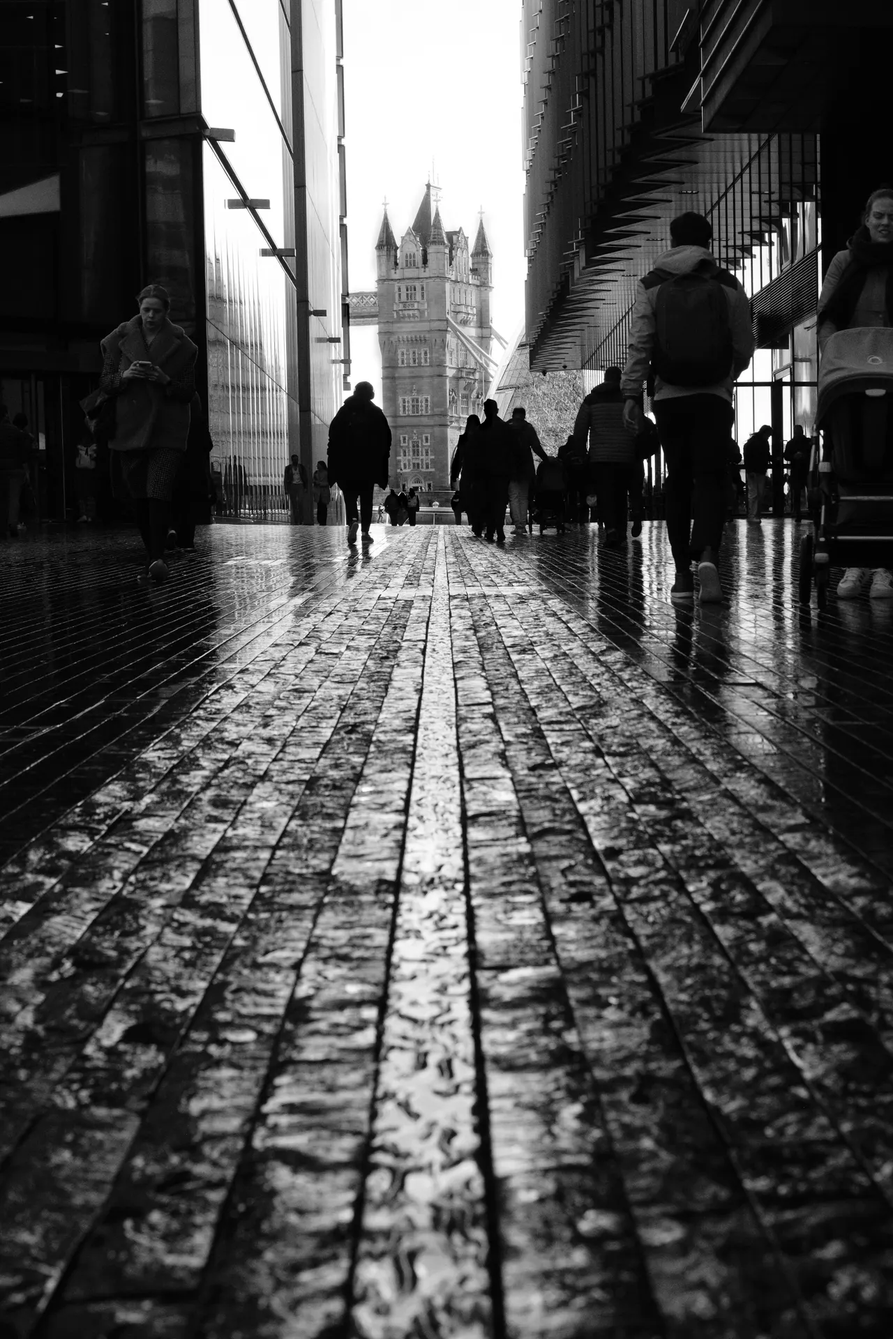 Wet cobbles reflecting the light, people walking toward Tower Bridge, black and white