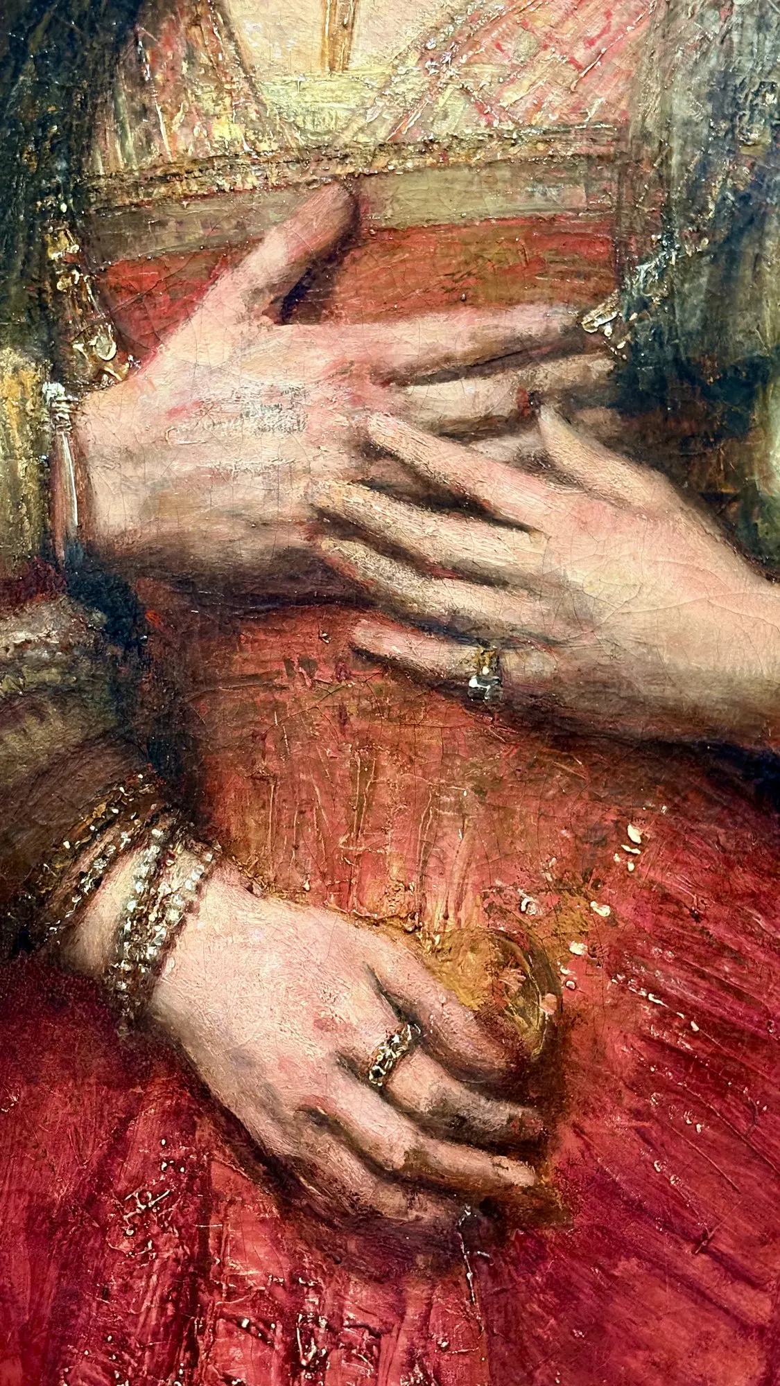 Hands resting on a red dress, bracelets and rings, detail from The Jewish Bride