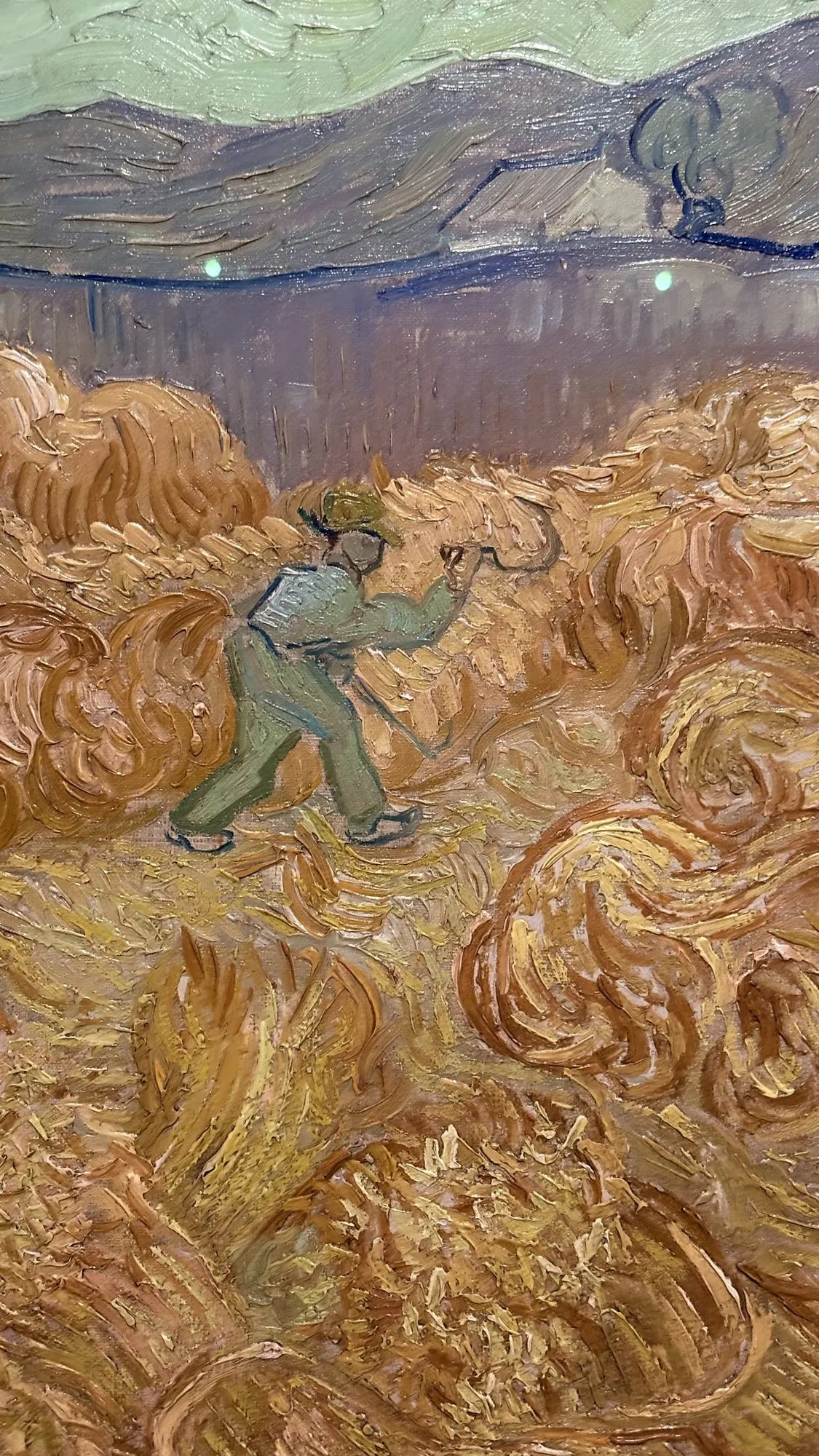 Moissonneur en vert au milieu de gerbes orange, montagnes au fond