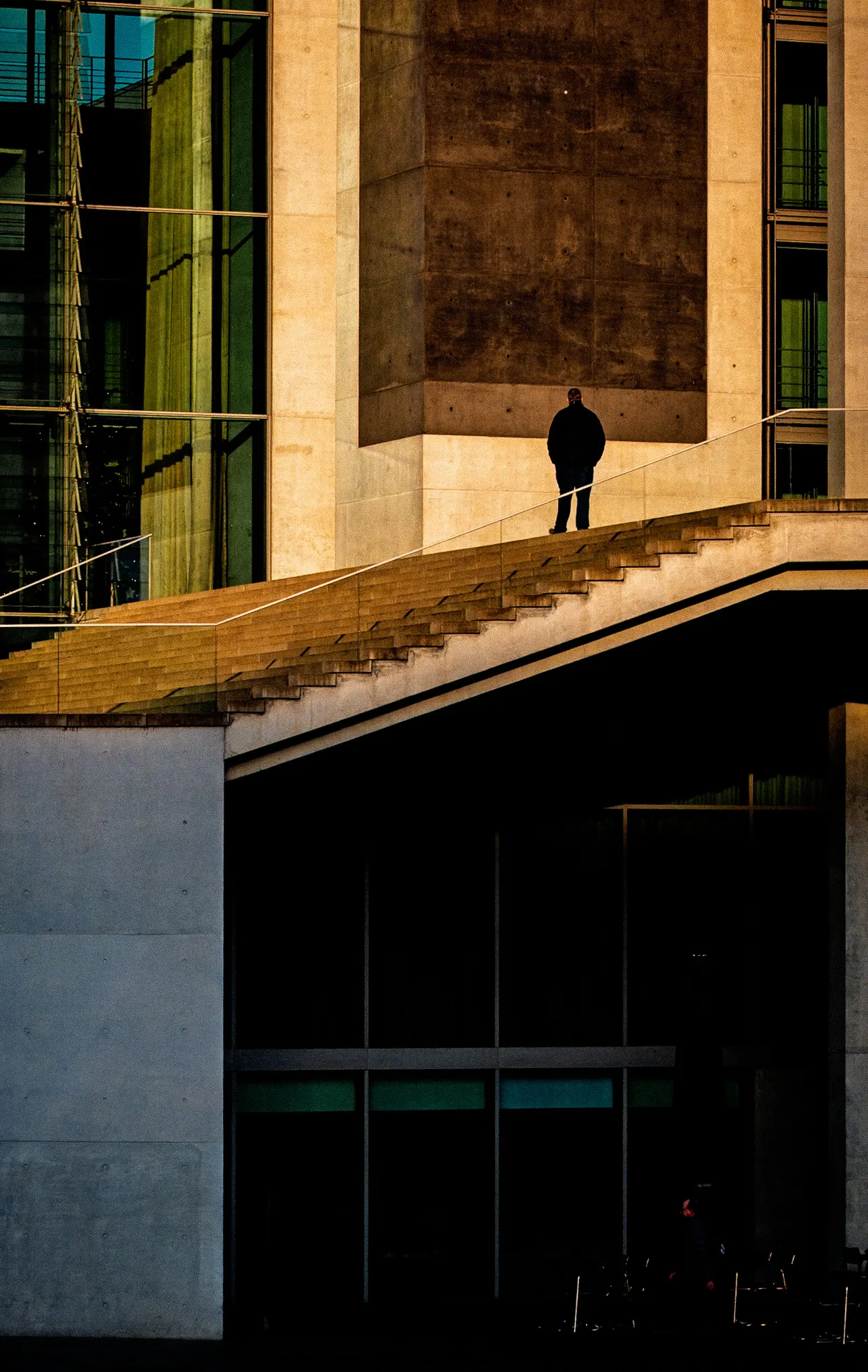 Silhouette seule en haut d'un escalier, façade de verre et de pierre