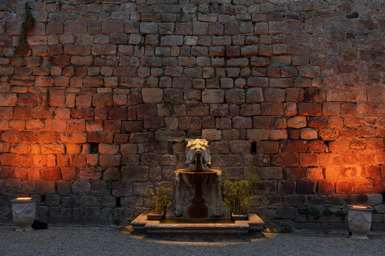 Stone fountain at the foot of a large sandstone wall backlit in orange, Fontfroide Abbey.