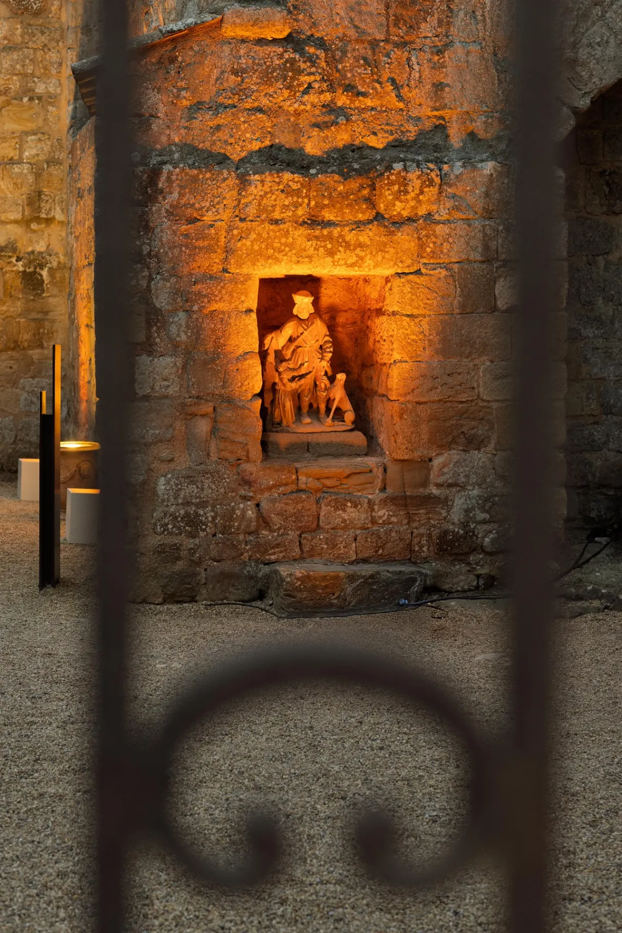 Statue of a pilgrim saint in a stone niche lit in warm light, Fontfroide Abbey at night.