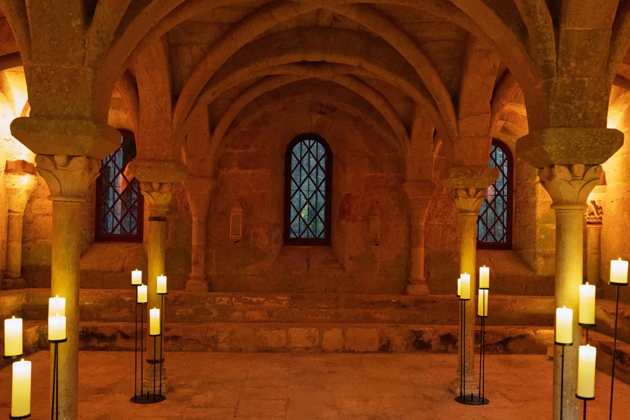 Romanesque chapter house lit by tall candles on metal stands, Fontfroide Abbey.