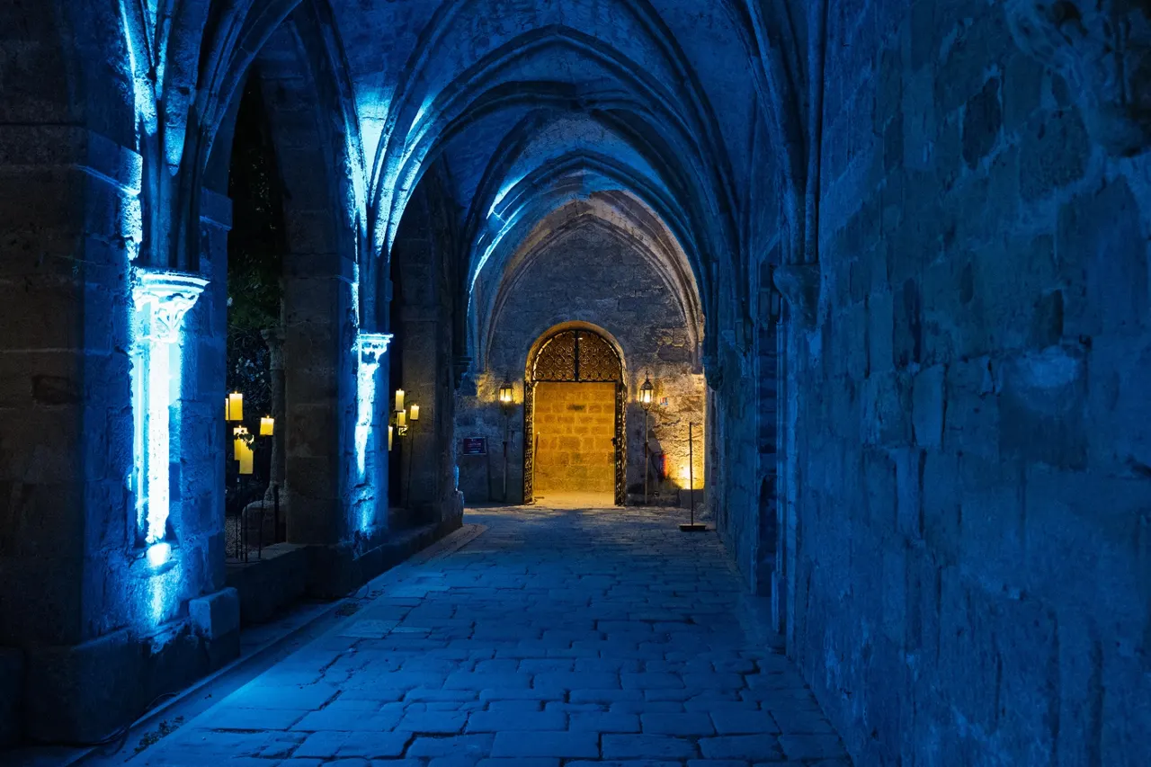 Vaulted cloister passage lit in blue opening onto a wooden door in warm light, Fontfroide Abbey.