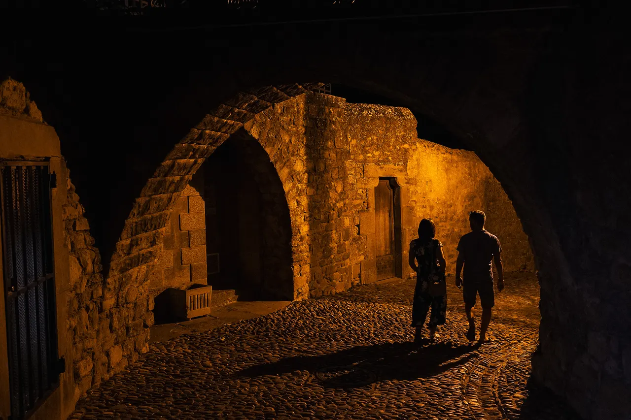 Deux silhouettes sous une arche éclairée, Cité de Carcassonne la nuit