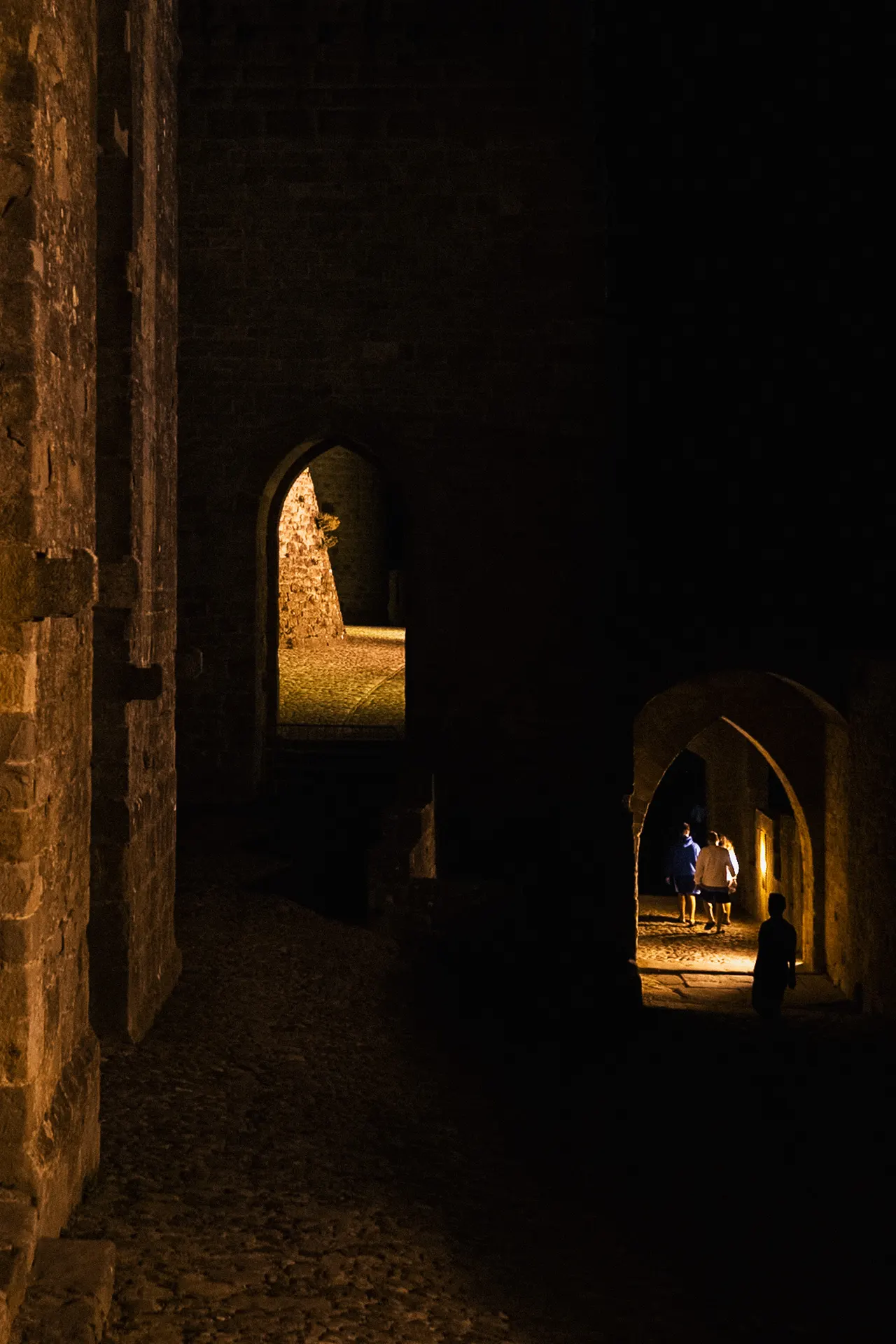 Passants sous une porte en ogive, au fond d'un passage sombre