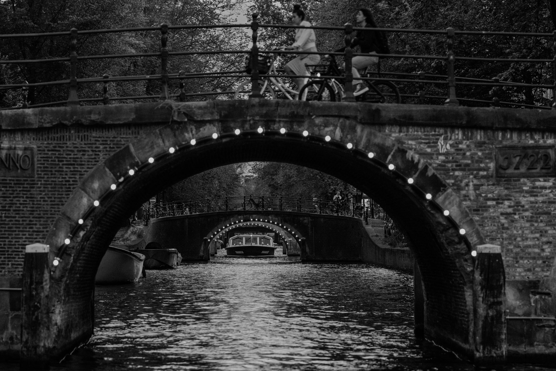 Amsterdam Night — two lit Reguliersgracht bridges, a boat passing under the arches